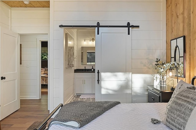 bedroom featuring sink, a barn door, dark hardwood / wood-style floors, ensuite bathroom, and wooden walls