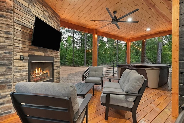 wooden deck with ceiling fan, a hot tub, and an outdoor stone fireplace