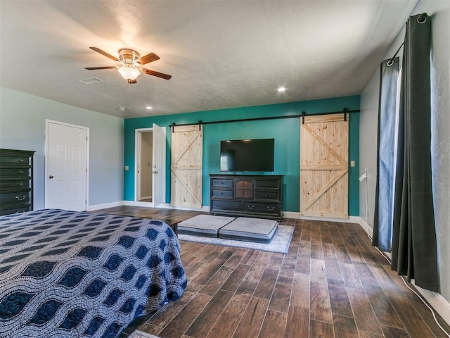 unfurnished bedroom featuring ceiling fan, a barn door, and dark hardwood / wood-style floors