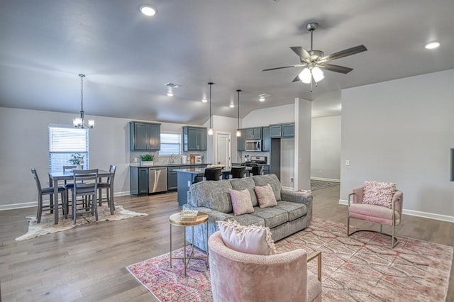 living room featuring ceiling fan with notable chandelier, light hardwood / wood-style flooring, and vaulted ceiling