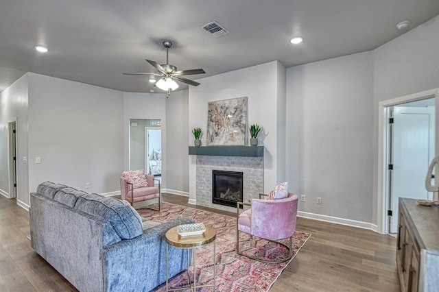 living room with hardwood / wood-style flooring, a brick fireplace, and ceiling fan