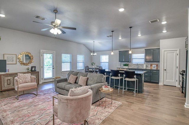 living room featuring light hardwood / wood-style flooring, ceiling fan with notable chandelier, lofted ceiling, and sink