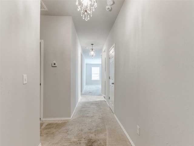 corridor with light colored carpet and a notable chandelier