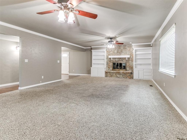 unfurnished living room with carpet, built in shelves, ceiling fan, crown molding, and a stone fireplace