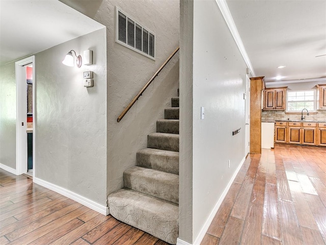 staircase with hardwood / wood-style floors, crown molding, and sink