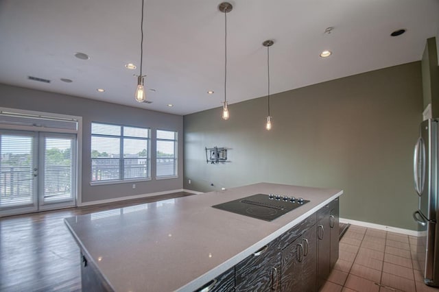 kitchen with tile patterned floors, black electric cooktop, decorative light fixtures, a kitchen island, and stainless steel refrigerator