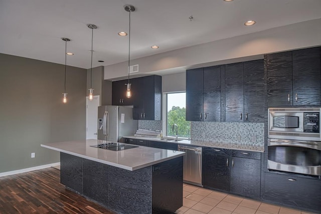 kitchen with light hardwood / wood-style flooring, backsplash, decorative light fixtures, a kitchen island, and appliances with stainless steel finishes