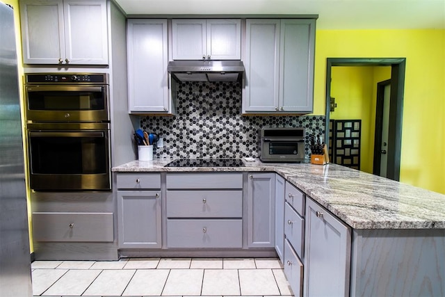 kitchen with tasteful backsplash, light stone counters, double oven, gray cabinets, and black electric cooktop