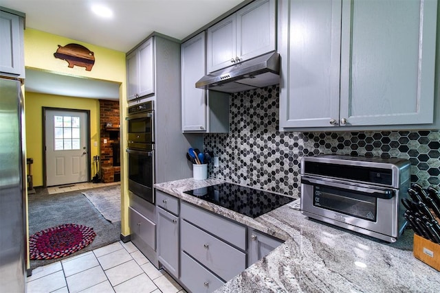 kitchen featuring light stone countertops, backsplash, stainless steel appliances, and gray cabinetry