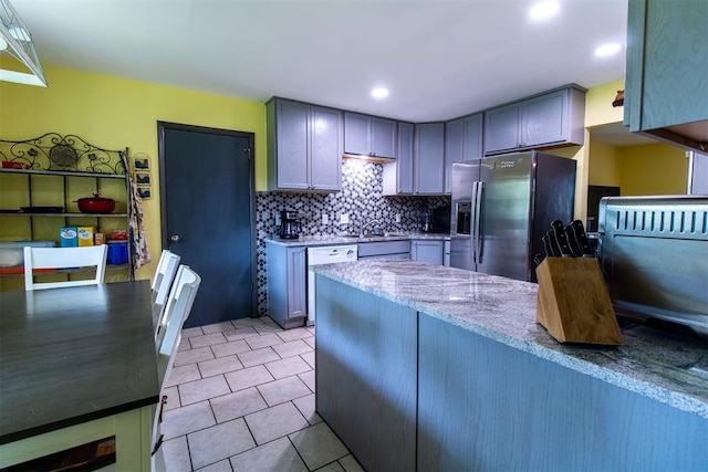 kitchen with appliances with stainless steel finishes, tasteful backsplash, light stone counters, gray cabinetry, and sink