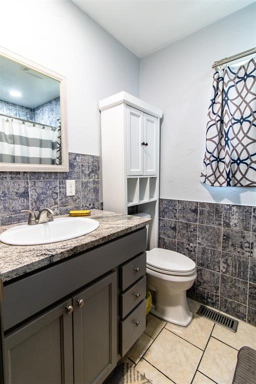 bathroom featuring tile patterned flooring, vanity, toilet, and tile walls