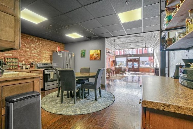 dining space with a drop ceiling, brick wall, and hardwood / wood-style flooring