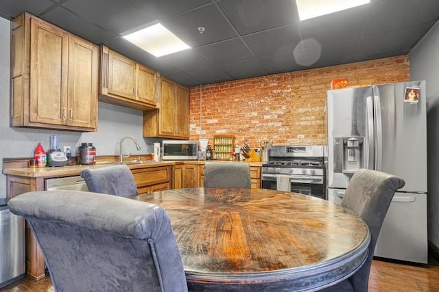 kitchen with appliances with stainless steel finishes, a paneled ceiling, brick wall, sink, and hardwood / wood-style floors