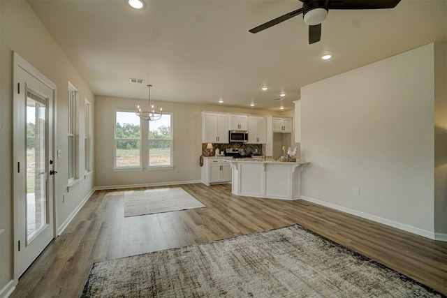 interior space with stainless steel appliances, light hardwood / wood-style flooring, decorative light fixtures, white cabinets, and ceiling fan with notable chandelier