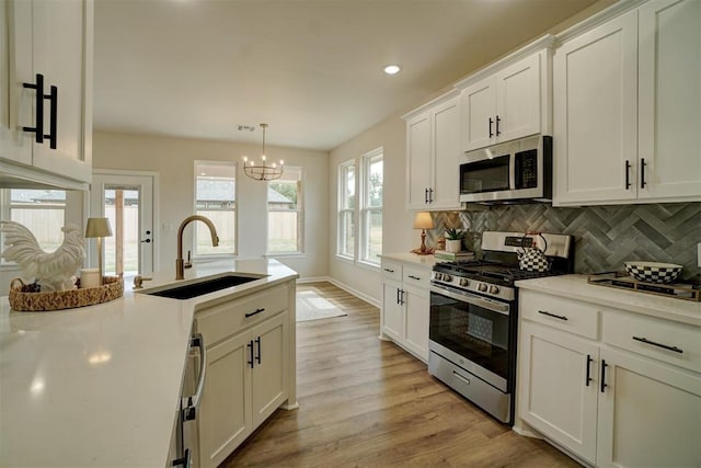 kitchen featuring stainless steel appliances, sink, pendant lighting, light hardwood / wood-style flooring, and white cabinetry