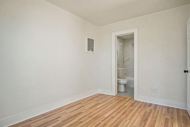 unfurnished bedroom with light wood-type flooring, electric panel, and ensuite bath