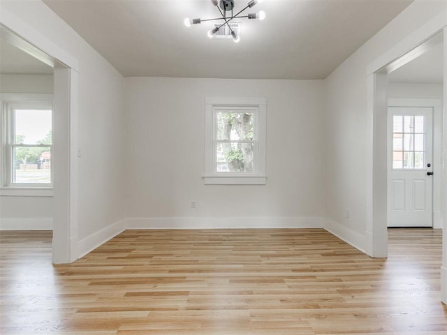 spare room with a notable chandelier, plenty of natural light, and light hardwood / wood-style flooring