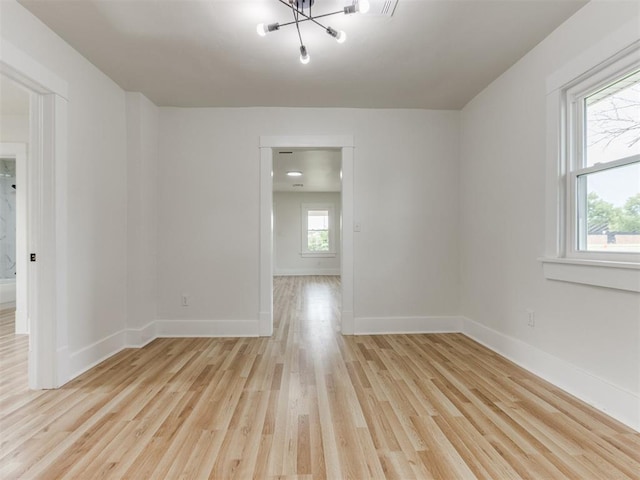 empty room with a chandelier, a wealth of natural light, and light hardwood / wood-style floors