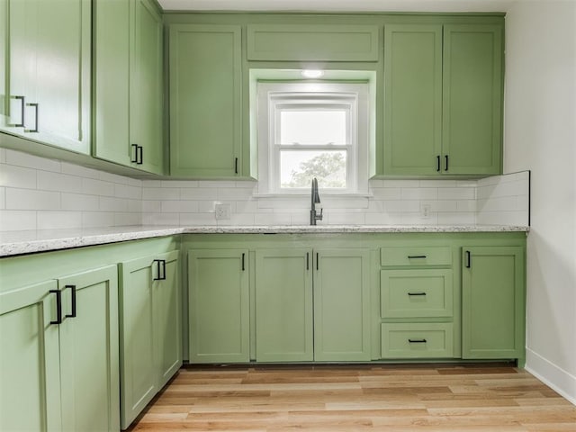 kitchen featuring sink, tasteful backsplash, light stone counters, light wood-type flooring, and green cabinetry