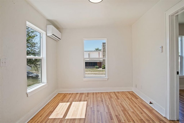 unfurnished room with light wood-type flooring, an AC wall unit, and a wealth of natural light