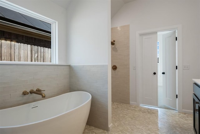 bathroom with vanity, vaulted ceiling, a tub to relax in, and tile walls