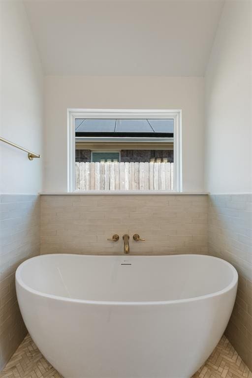 bathroom featuring a tub to relax in, a wealth of natural light, and tile walls