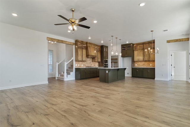 kitchen featuring backsplash, light wood-type flooring, an island with sink, and hanging light fixtures