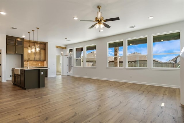 unfurnished living room with sink, ceiling fan with notable chandelier, and hardwood / wood-style flooring