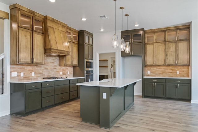 kitchen with pendant lighting, light wood-type flooring, premium range hood, and a kitchen island with sink