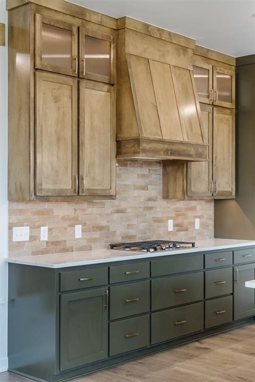 kitchen featuring light wood-type flooring, premium range hood, stainless steel gas cooktop, and backsplash