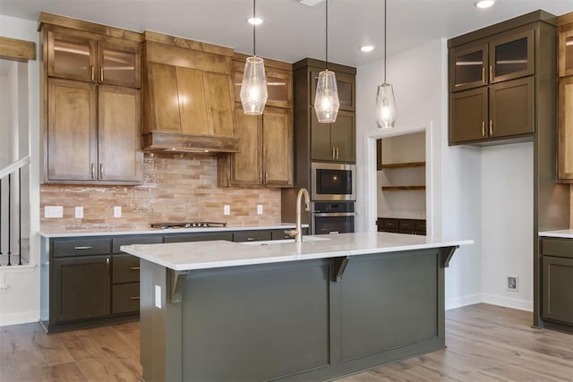 kitchen with appliances with stainless steel finishes, light wood-type flooring, a center island with sink, and sink