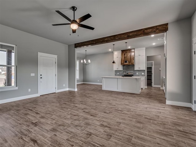 unfurnished living room with beam ceiling, ceiling fan with notable chandelier, light hardwood / wood-style floors, and sink