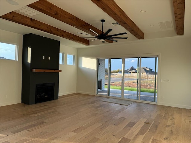 unfurnished living room featuring beamed ceiling, a large fireplace, light hardwood / wood-style flooring, and a healthy amount of sunlight