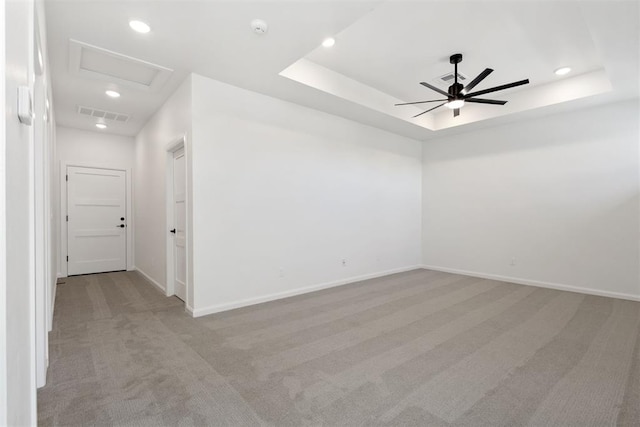 empty room with light carpet, visible vents, attic access, and a raised ceiling