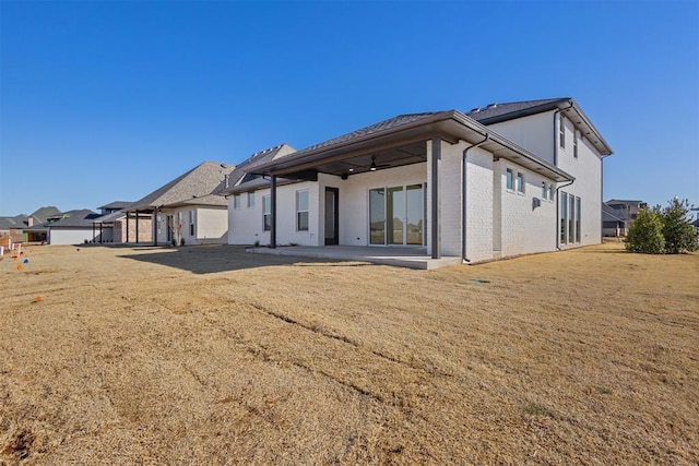 back of house with brick siding, a patio area, and a lawn