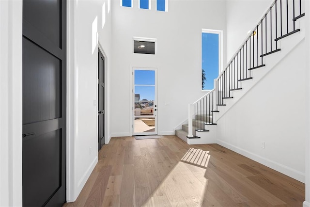 foyer entrance featuring stairway, baseboards, a towering ceiling, and wood finished floors