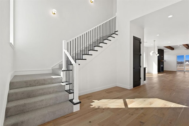 stairway with a towering ceiling, recessed lighting, baseboards, and wood finished floors