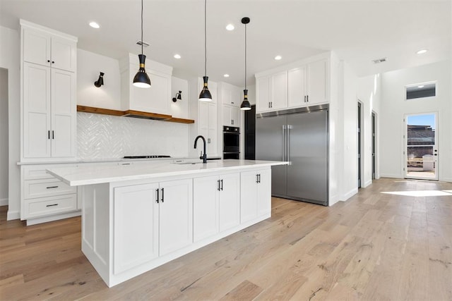 kitchen with cooktop, white cabinets, stainless steel built in fridge, and a sink