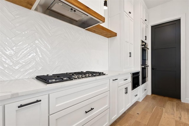 kitchen with under cabinet range hood, backsplash, appliances with stainless steel finishes, white cabinets, and light wood finished floors