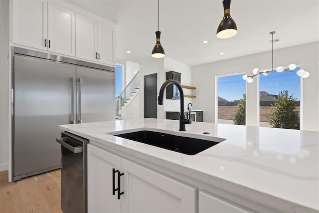 kitchen featuring pendant lighting, stainless steel built in refrigerator, a sink, white cabinetry, and light wood-style floors