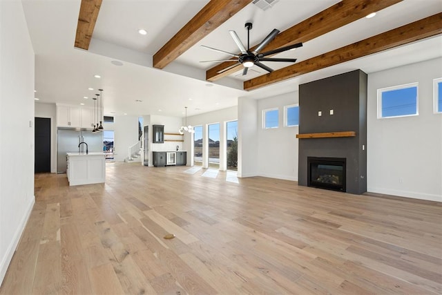 unfurnished living room with baseboards, beamed ceiling, ceiling fan with notable chandelier, a fireplace, and light wood-style floors