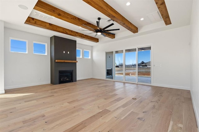 unfurnished living room with a healthy amount of sunlight, a large fireplace, baseboards, beamed ceiling, and light wood-type flooring