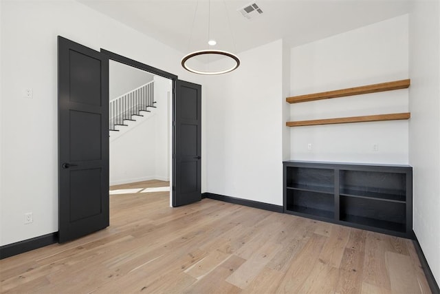 unfurnished room with stairs, baseboards, visible vents, and light wood-type flooring