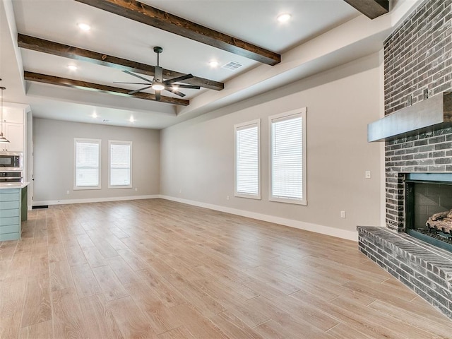 unfurnished living room with beamed ceiling, a brick fireplace, light hardwood / wood-style flooring, and ceiling fan