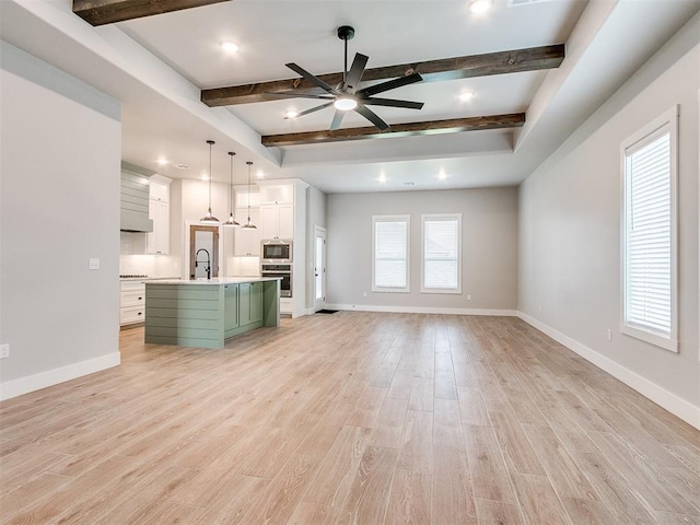 unfurnished living room with beamed ceiling, ceiling fan, and light hardwood / wood-style floors