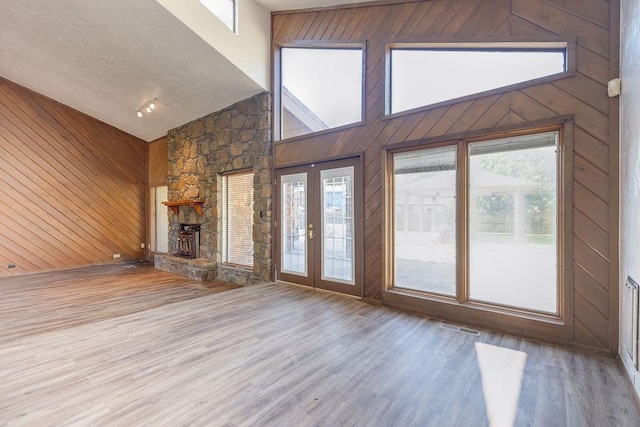 unfurnished living room with high vaulted ceiling, wood-type flooring, and wooden walls