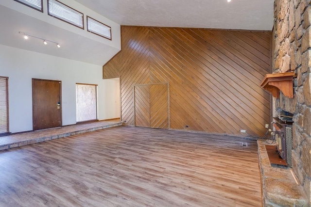 unfurnished living room featuring wooden walls, light hardwood / wood-style flooring, and high vaulted ceiling