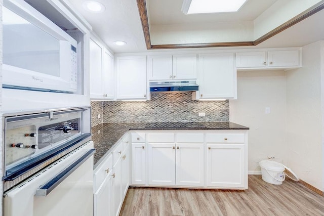 kitchen featuring white cabinets, light wood-type flooring, white appliances, and dark stone countertops