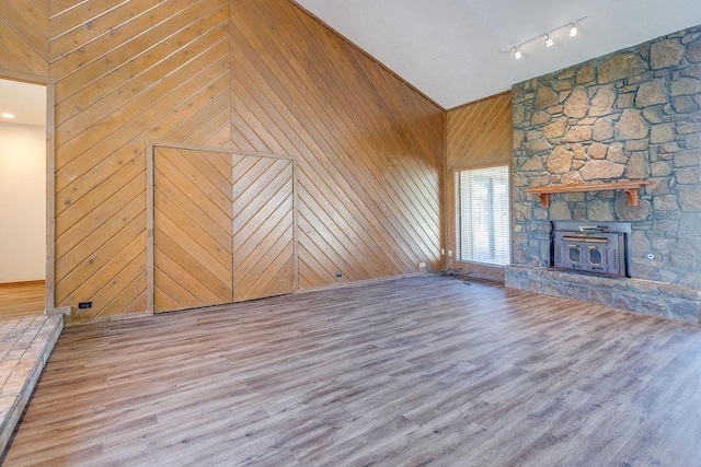 unfurnished living room featuring rail lighting, light hardwood / wood-style floors, high vaulted ceiling, and wooden walls