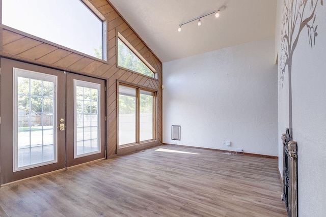 empty room with light wood-type flooring, high vaulted ceiling, and french doors